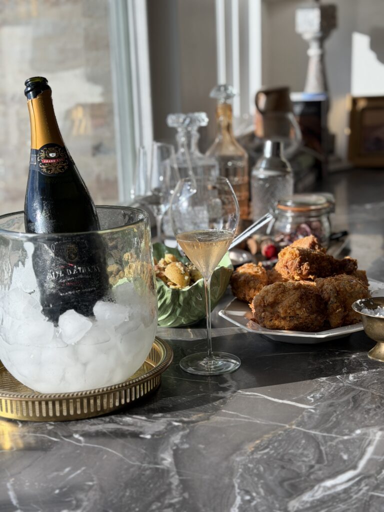 Champagne in a bucket of ice, a glass poured, crispy fried chicken and potato salad